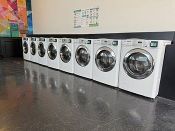 A row of white front load washing machines are lined up on a counter.